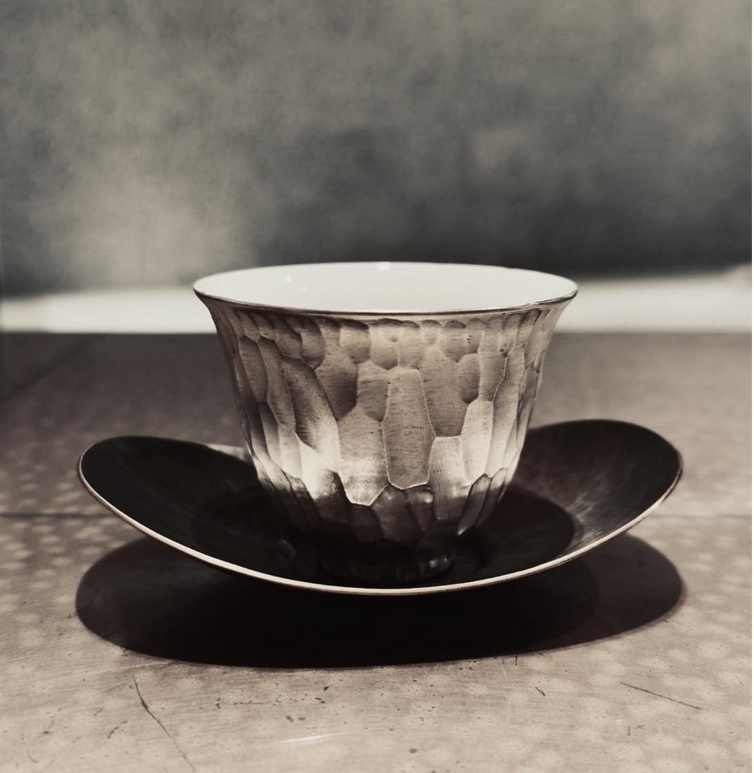 A hand-carved tea cup on a dark saucer in soft light